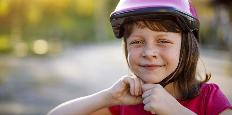Happy cute girl putting cycle helmet on